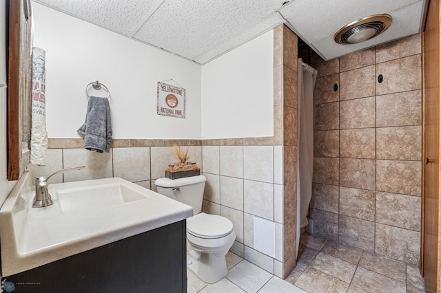 bathroom with toilet, tile walls, a shower with curtain, vanity, and tile patterned floors