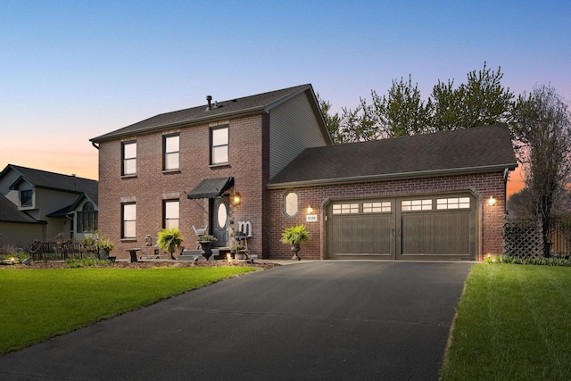 colonial home with a garage, driveway, a lawn, and brick siding