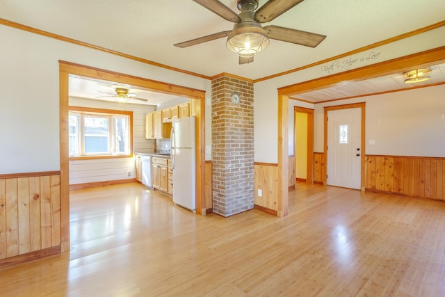 unfurnished living room with wooden walls, light wood finished floors, ceiling fan, and a wainscoted wall