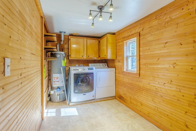 laundry area with cabinet space, water heater, wooden walls, and washing machine and clothes dryer