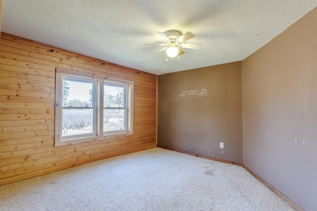 spare room with carpet, a ceiling fan, a textured ceiling, wood walls, and baseboards