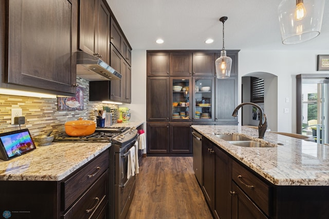 kitchen featuring under cabinet range hood, a sink, stainless steel appliances, arched walkways, and dark wood-style flooring