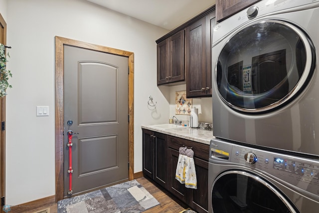 laundry area featuring stacked washer / drying machine, cabinet space, and wood finished floors