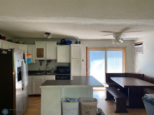 kitchen featuring stainless steel fridge with ice dispenser, a sink, black microwave, a ceiling fan, and white cabinets