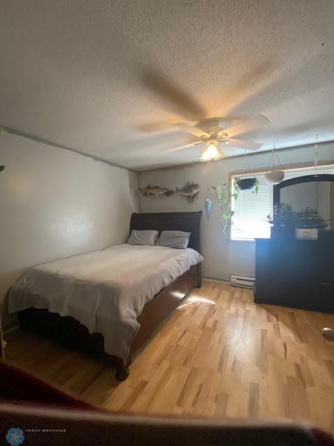 bedroom featuring wood finished floors, a textured ceiling, a baseboard heating unit, and ceiling fan