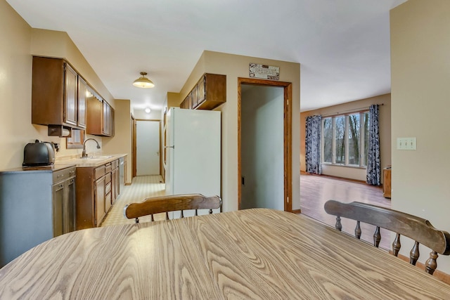 kitchen featuring a sink, freestanding refrigerator, brown cabinetry, stainless steel dishwasher, and light countertops