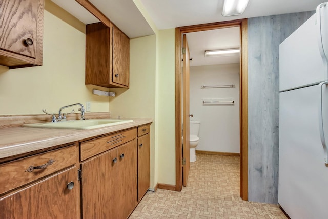 interior space with a sink, brown cabinets, freestanding refrigerator, light floors, and light countertops