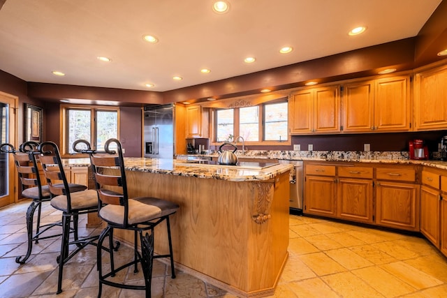 kitchen with light stone counters, recessed lighting, a kitchen bar, a center island, and appliances with stainless steel finishes