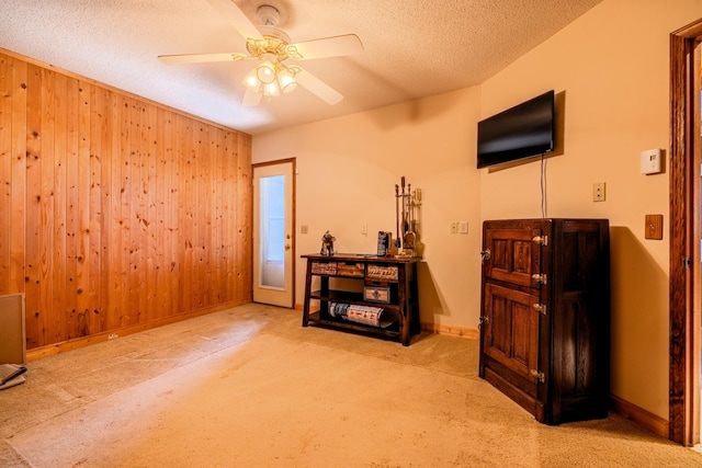 interior space featuring a ceiling fan, a textured ceiling, carpet, baseboards, and wood walls