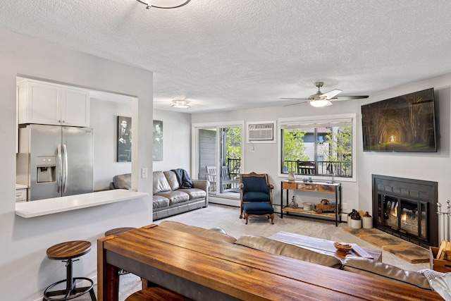 living area with ceiling fan, a textured ceiling, a glass covered fireplace, light carpet, and baseboard heating