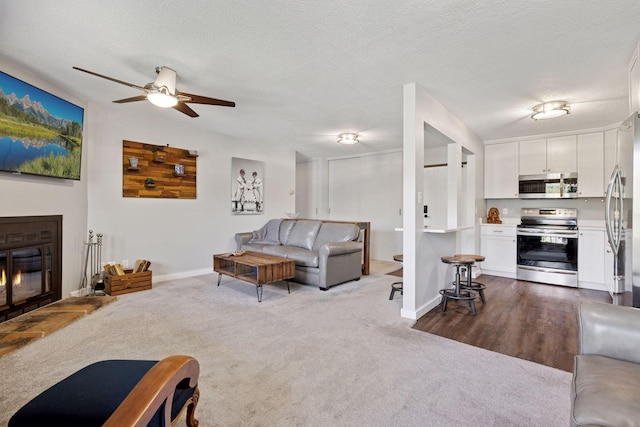 living room with a ceiling fan, dark carpet, a glass covered fireplace, baseboards, and a textured ceiling