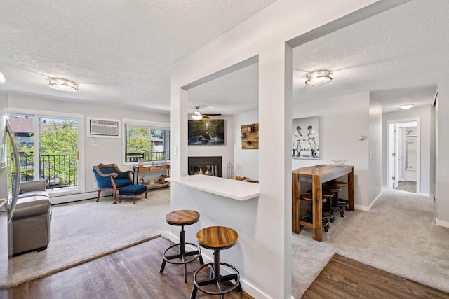 living room with a textured ceiling, a warm lit fireplace, a ceiling fan, a wall mounted AC, and baseboards