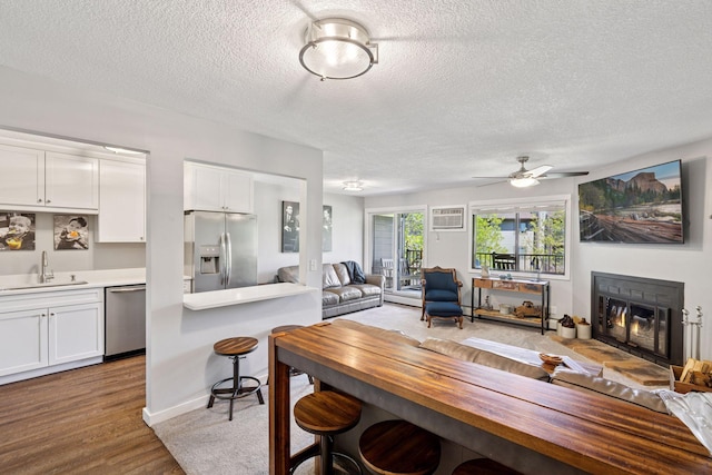 dining space with a textured ceiling, a glass covered fireplace, ceiling fan, a wall mounted AC, and wood finished floors