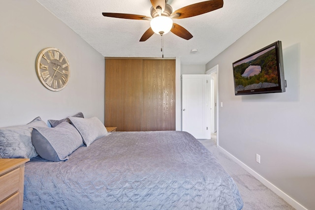 bedroom featuring light colored carpet, baseboards, a closet, a ceiling fan, and a textured ceiling