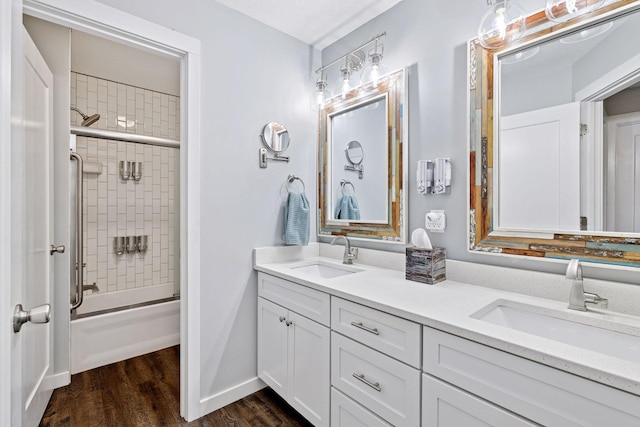 bathroom featuring wood finished floors, double vanity, shower / bath combination with glass door, and baseboards
