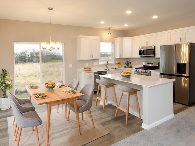 kitchen featuring appliances with stainless steel finishes, a sink, a center island, a chandelier, and white cabinetry