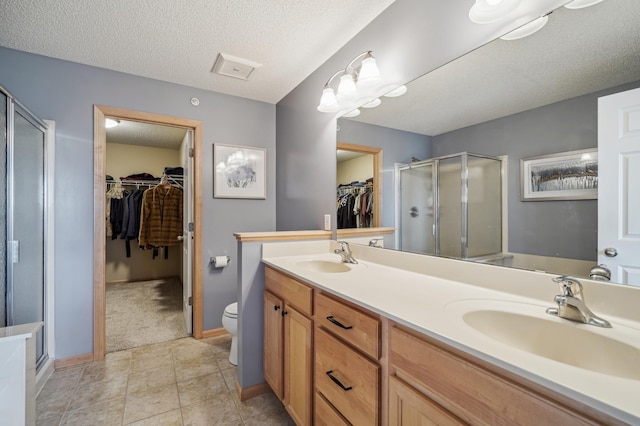 full bath with a shower stall, a textured ceiling, double vanity, toilet, and baseboards