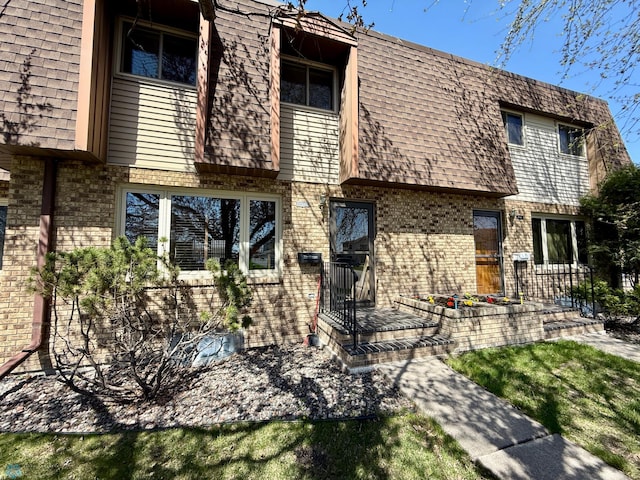 back of property with mansard roof, roof with shingles, and brick siding