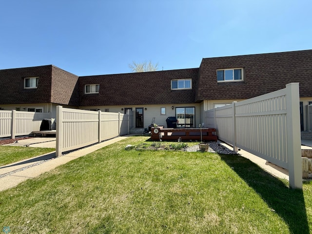 back of property with a lawn, roof with shingles, fence, and mansard roof