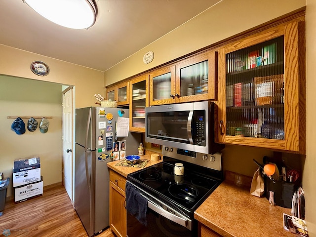 kitchen featuring brown cabinets, appliances with stainless steel finishes, light countertops, glass insert cabinets, and light wood-style floors