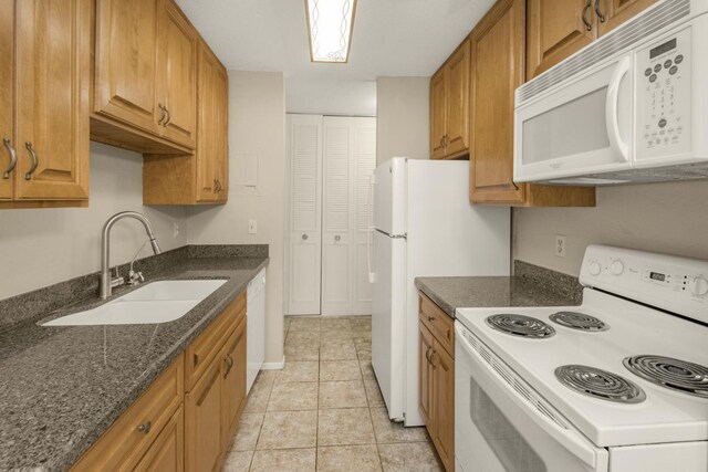 kitchen with white appliances, a sink, brown cabinets, dark stone countertops, and light tile patterned floors