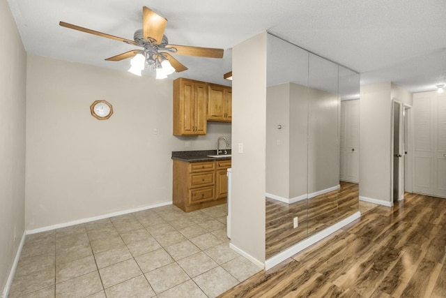 kitchen with a sink, dark countertops, a ceiling fan, and baseboards
