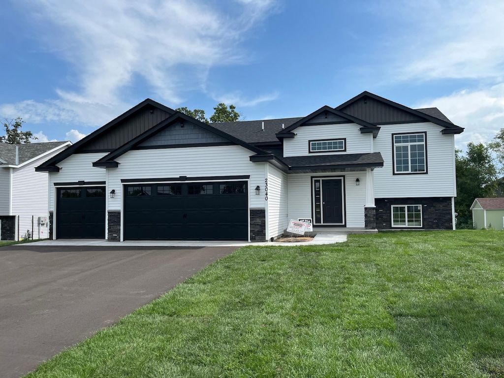 split level home with aphalt driveway, a garage, stone siding, a front yard, and roof with shingles