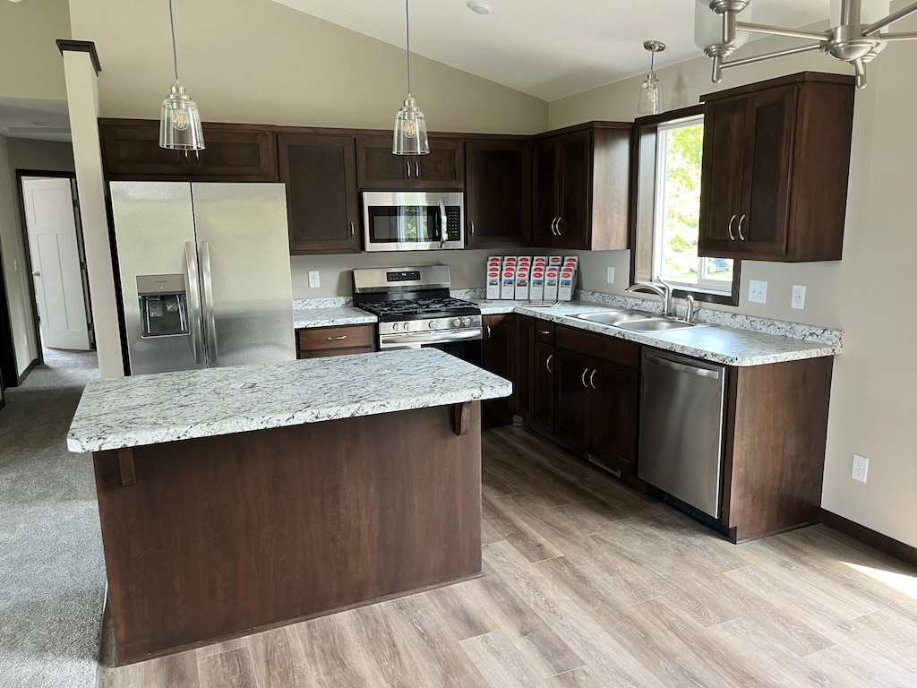 kitchen with decorative light fixtures, dark brown cabinetry, a sink, vaulted ceiling, and appliances with stainless steel finishes