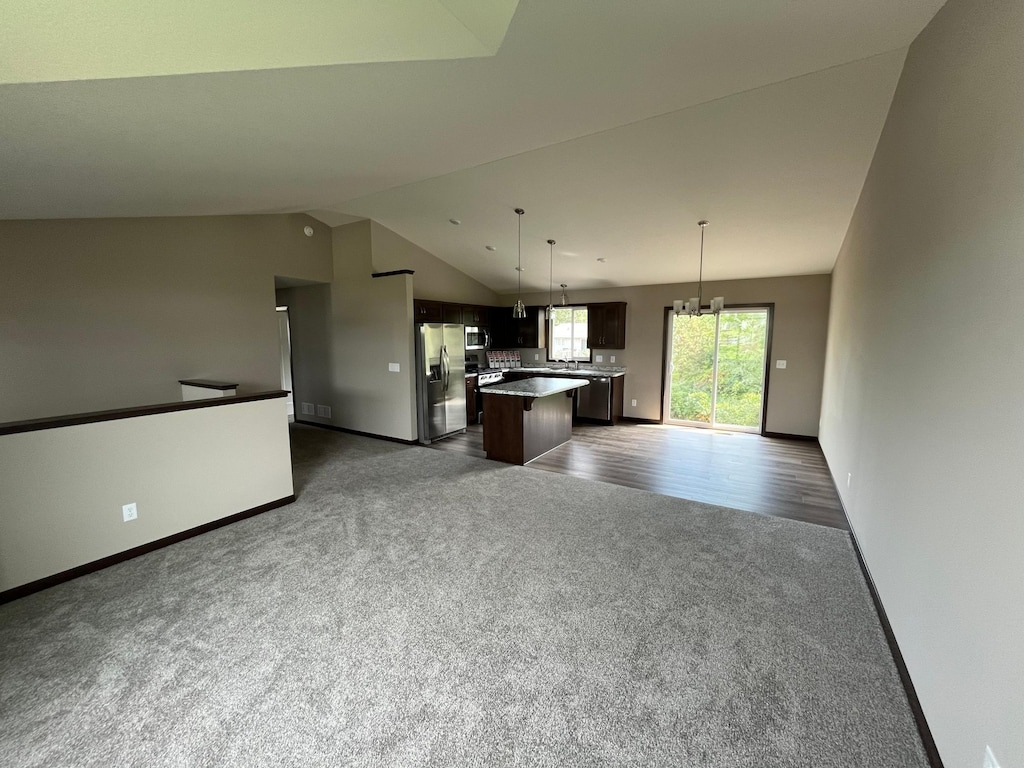kitchen featuring lofted ceiling, open floor plan, a kitchen island, dark carpet, and stainless steel appliances