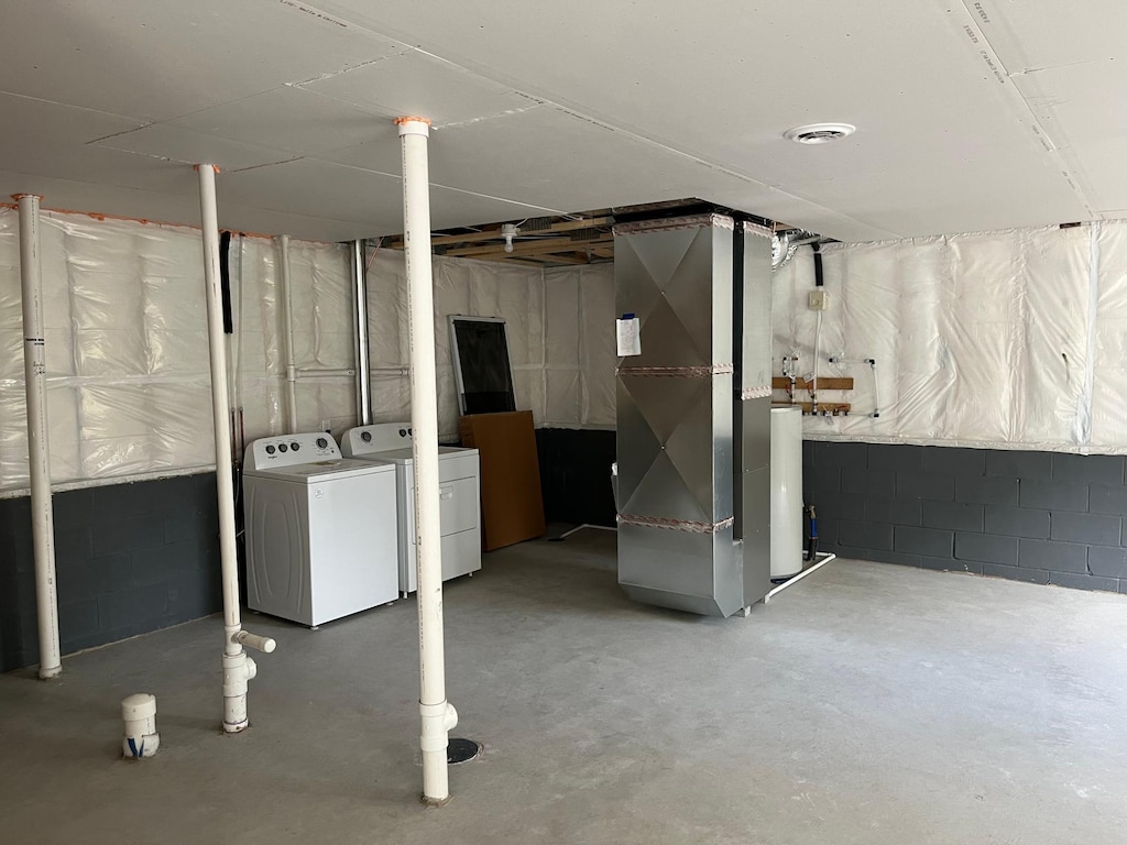 unfinished below grade area featuring independent washer and dryer, heating unit, and concrete block wall