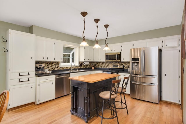 kitchen featuring a sink, white cabinetry, light wood-style floors, stainless steel appliances, and tasteful backsplash