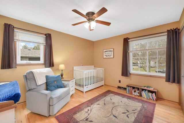 bedroom with a crib, light wood-type flooring, visible vents, and multiple windows