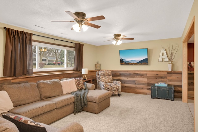 carpeted living area featuring wood walls, visible vents, ceiling fan, and a wainscoted wall