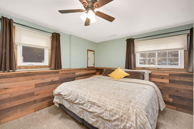 carpeted bedroom featuring a ceiling fan and wood walls