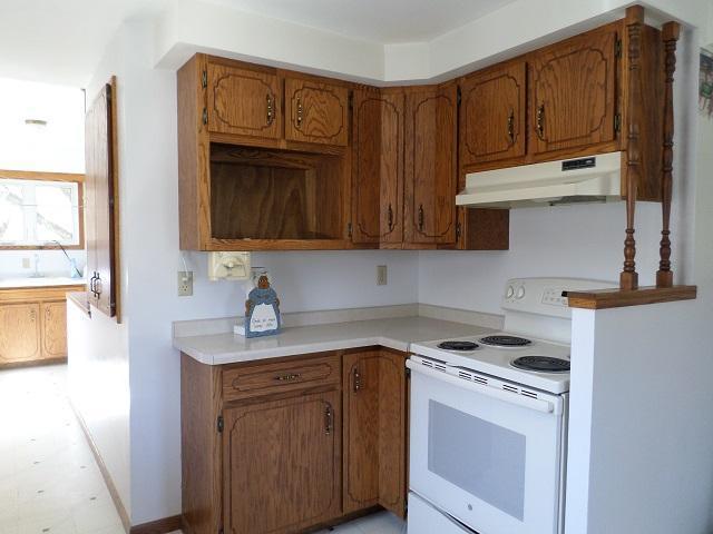 202 Buse Ave NE, Red Lake Falls, MN 56750 - kitchen with under cabinet range hood, light countertops, brown cabinetry, and white range with electric cooktop
