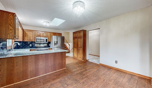 kitchen featuring a sink, a peninsula, wood finished floors, stainless steel appliances, and a skylight