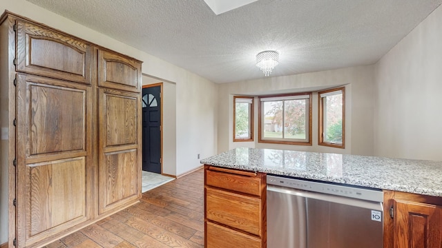 kitchen with light wood finished floors, dishwasher, a textured ceiling, and light stone countertops