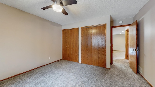 unfurnished bedroom with a textured ceiling, multiple closets, visible vents, ceiling fan, and carpet floors