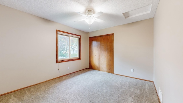 unfurnished bedroom with a closet, attic access, a textured ceiling, carpet, and baseboards