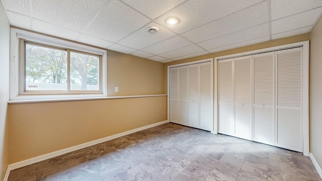 unfurnished bedroom featuring a paneled ceiling, two closets, and baseboards