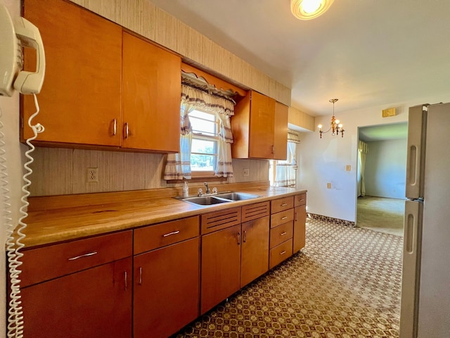 kitchen with freestanding refrigerator, a sink, light countertops, and a chandelier