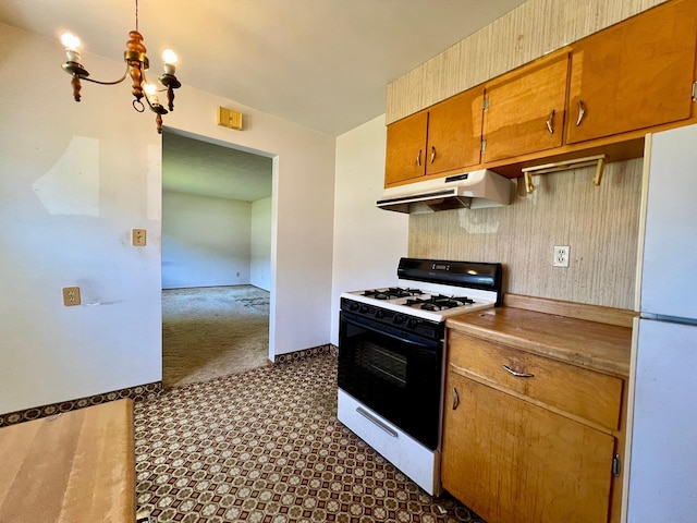 kitchen featuring gas range, under cabinet range hood, freestanding refrigerator, dark floors, and brown cabinetry
