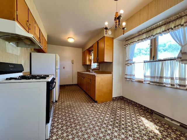 kitchen with gas stove, under cabinet range hood, baseboards, brown cabinets, and a chandelier