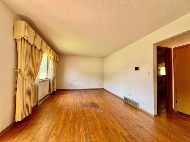 empty room with wood finished floors, a baseboard radiator, a textured ceiling, and baseboards