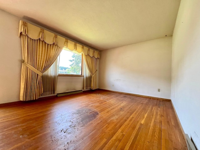 unfurnished room featuring a baseboard heating unit, hardwood / wood-style flooring, and baseboards