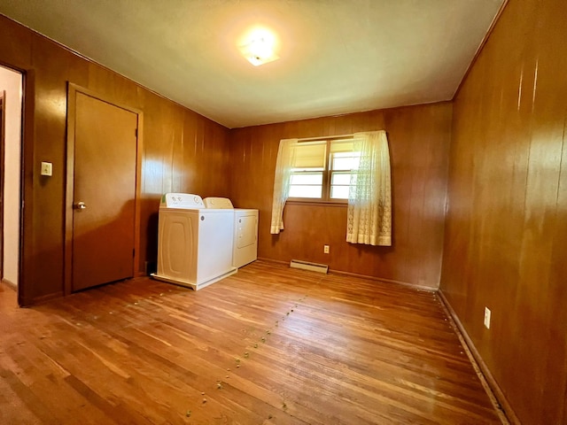 laundry room with washing machine and dryer, a baseboard heating unit, wood finished floors, and wooden walls