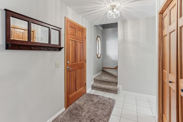 entryway with light tile patterned flooring, baseboards, stairway, and a textured ceiling