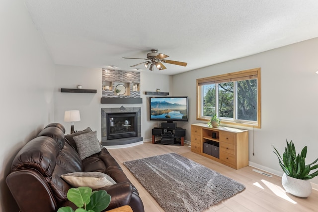 living room with a ceiling fan, a tile fireplace, light wood-type flooring, baseboards, and a textured ceiling