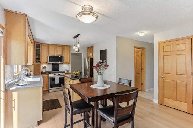 kitchen featuring appliances with stainless steel finishes, a sink, backsplash, glass insert cabinets, and light wood-style flooring