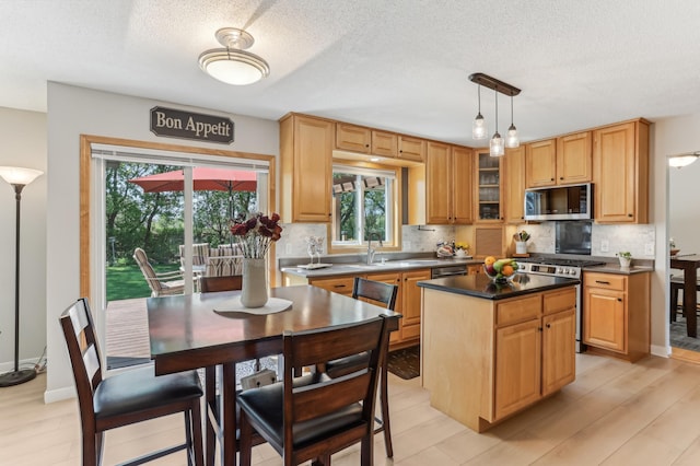 kitchen with appliances with stainless steel finishes, decorative backsplash, a center island, a sink, and a textured ceiling